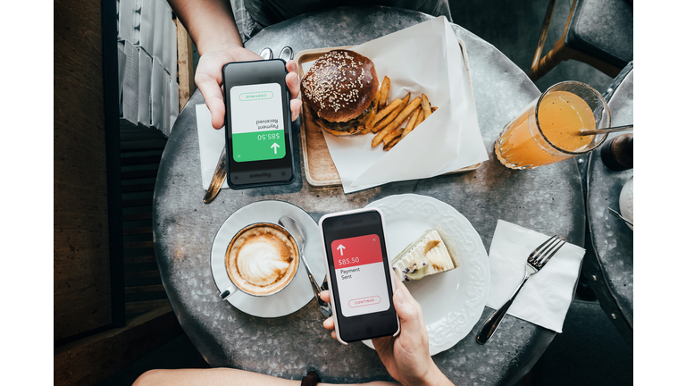 Overhead view of friends sending/receiving the payment of the meal through digital wallet device on smartphone while dining together in a restaurant