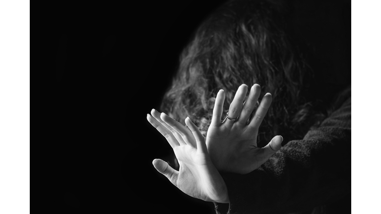 Violence against women. Black and white portrait of scared and desperate woman, focus on the hands in protective gesture