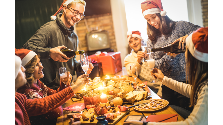 Friends group with santa hats celebrating Christmas with champagne and sweets food at home dinner - Winter holidays concept with people enjoying time and having fun eating together - Warm filter