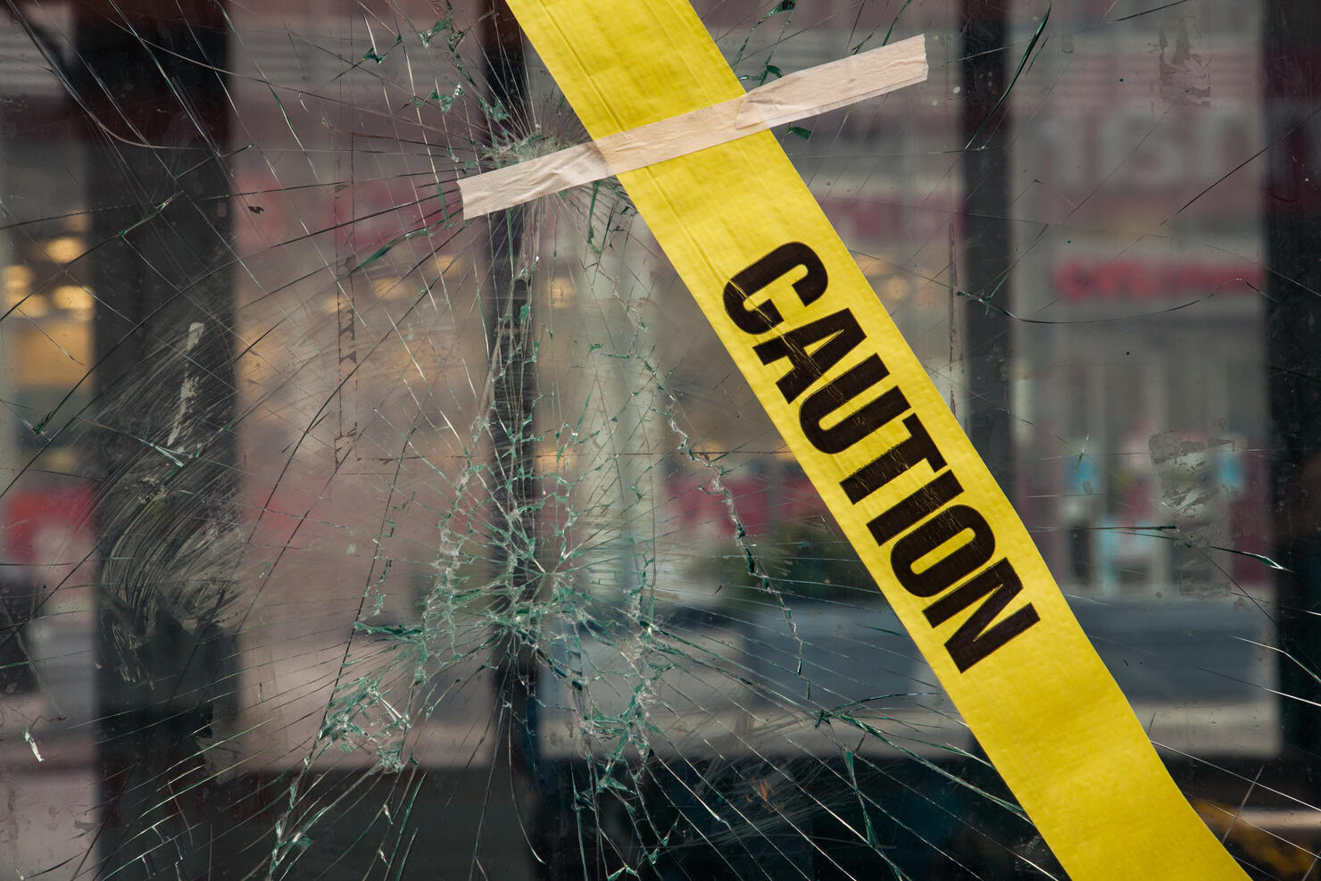 Broken window with glued yellow tape with "CAUTION" lettering