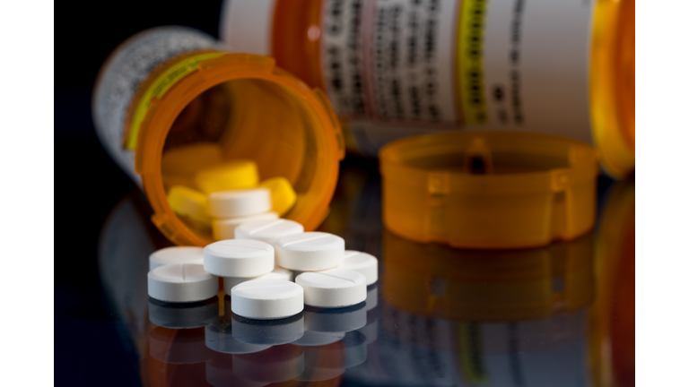 Macro of oxycodone opioid tablets with prescription bottles against dark background