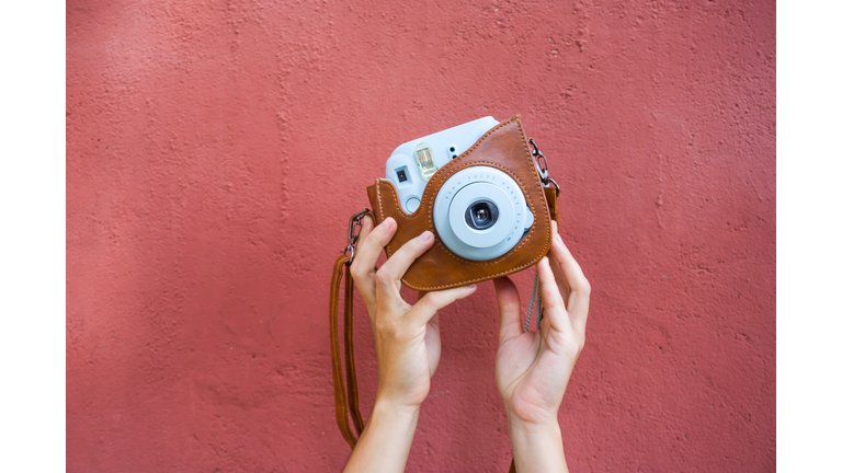 Woman hands holding a blue instax camera with a red wall on the background.