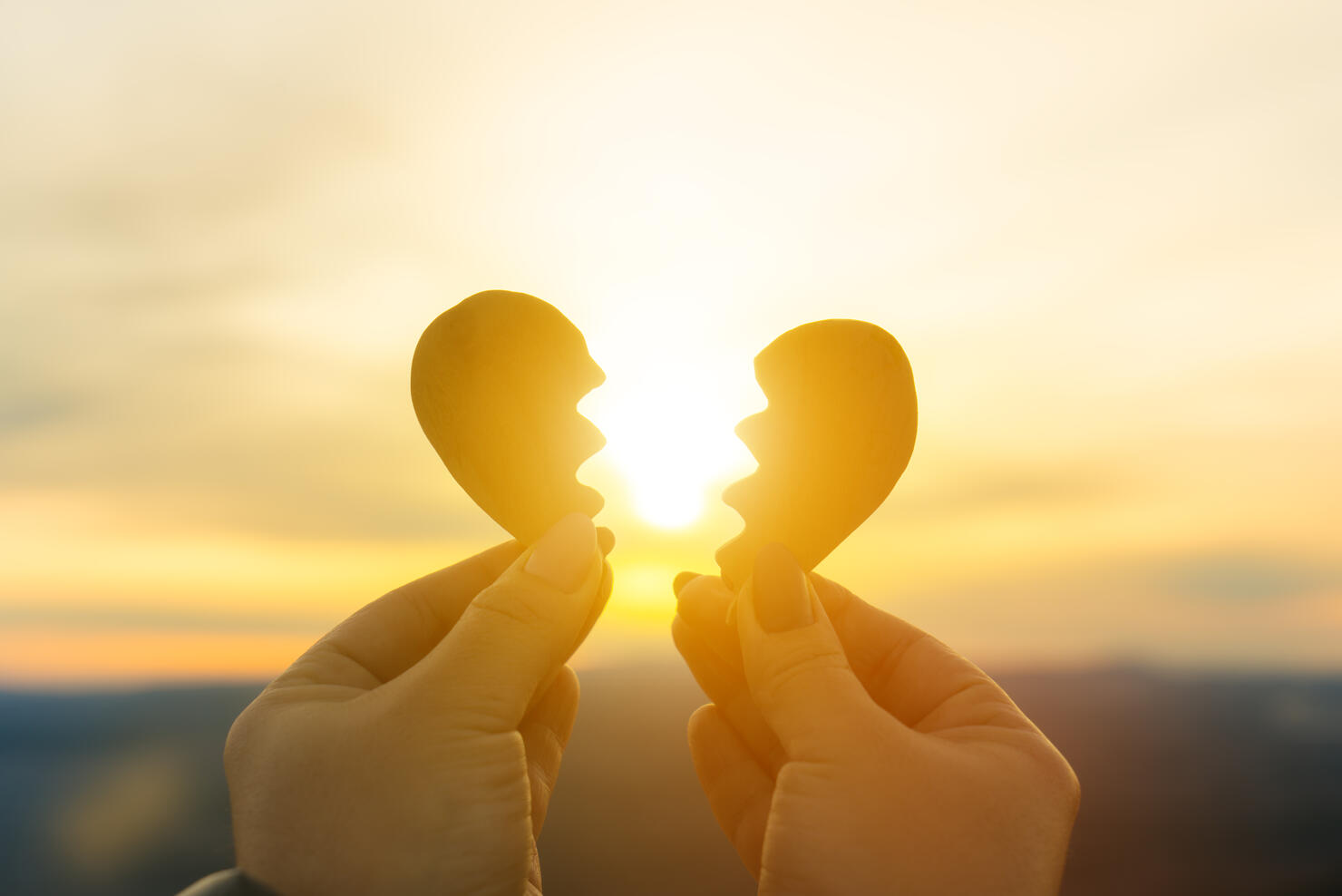 Two hands and a broken heart on a sunset background.