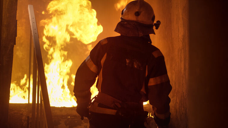 Building is On Fire. Fireman is Going Upstairs. Open Flames are Seen on Stairs.