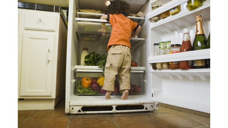 Boy standing in refrigerator looking for snack