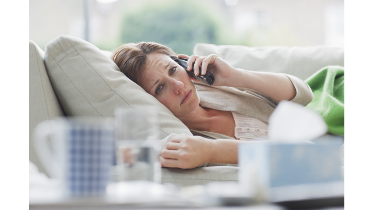 Sick woman laying on sofa talking on telephone