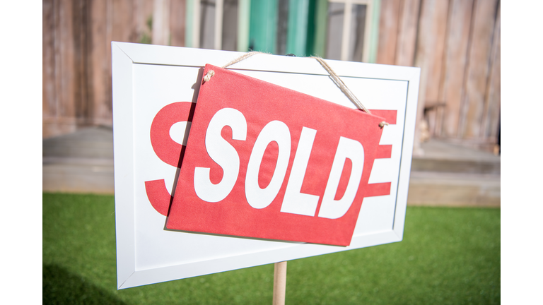 sale banner with sold card standing near new house