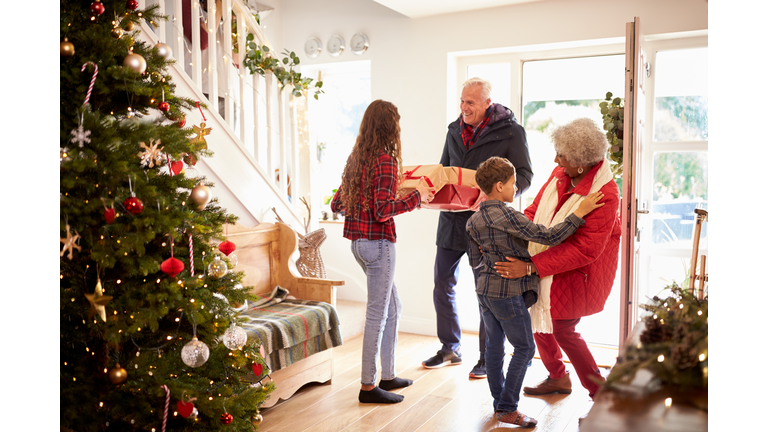 Excited Grandchildren Greeting Grandparents With Presents Visiting On Christmas Day