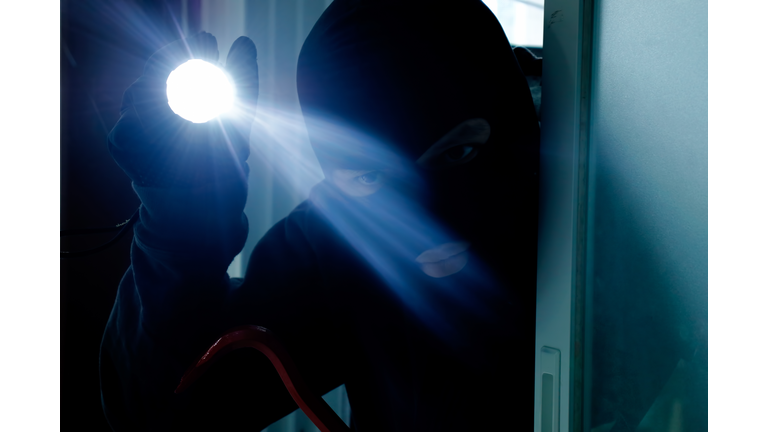 Masked burglar holding flashlight while secretly entering into a house