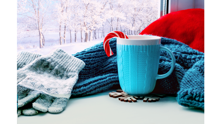 Christmas background. Winter background. Cup with candy cane, woolen scarf and grey gloves on windowsill