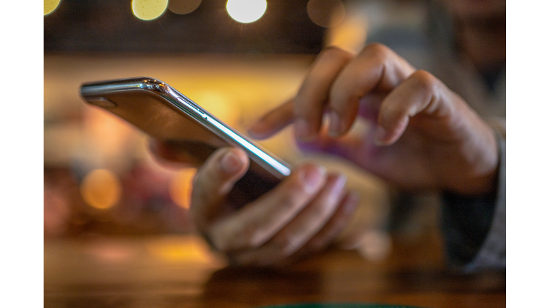 Closeup image of a man holding and using smart phone with coffee cup on wooden table in cafe