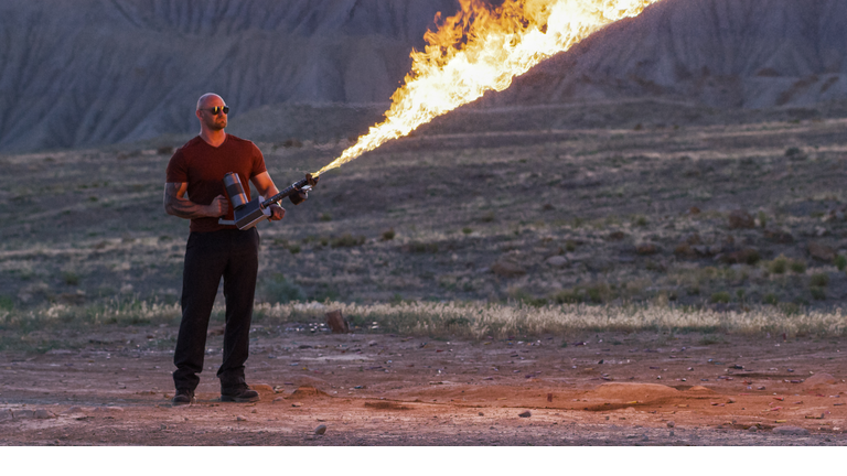 A Muscled Man Shoots a Flamethrower in a Desert