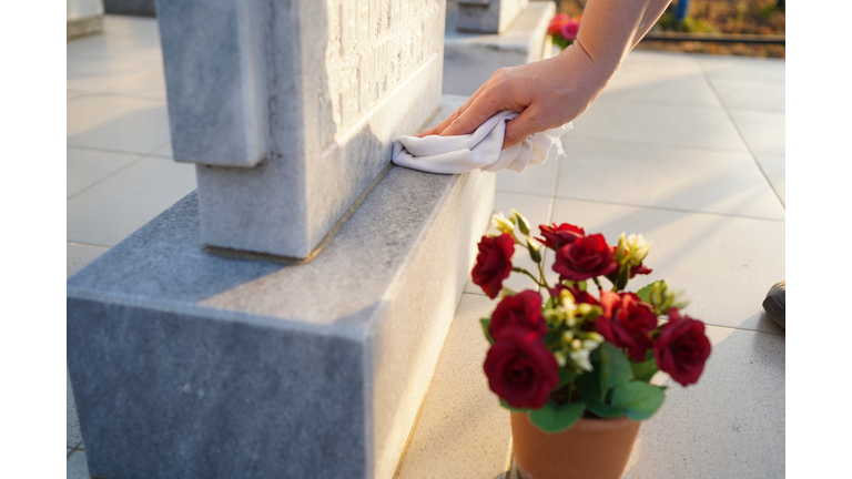 Cleaning cemetery. A woman's hand washes grey monument at the grave with rag