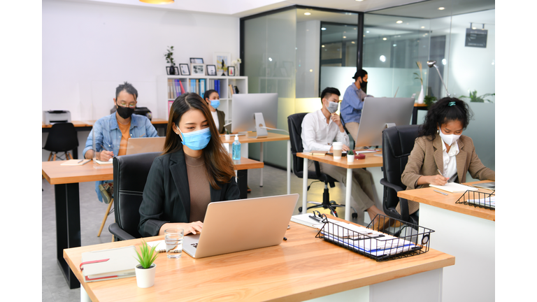 Asian office workers wearing face masks working in the new normal office and doing social distancing during coronavirus covid-19 pandemic