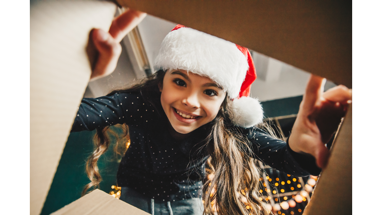 Surprised cute child girl opening a Christmas present. Little kid having fun near decorated tree indoors.  Happy  holidays and New Year.