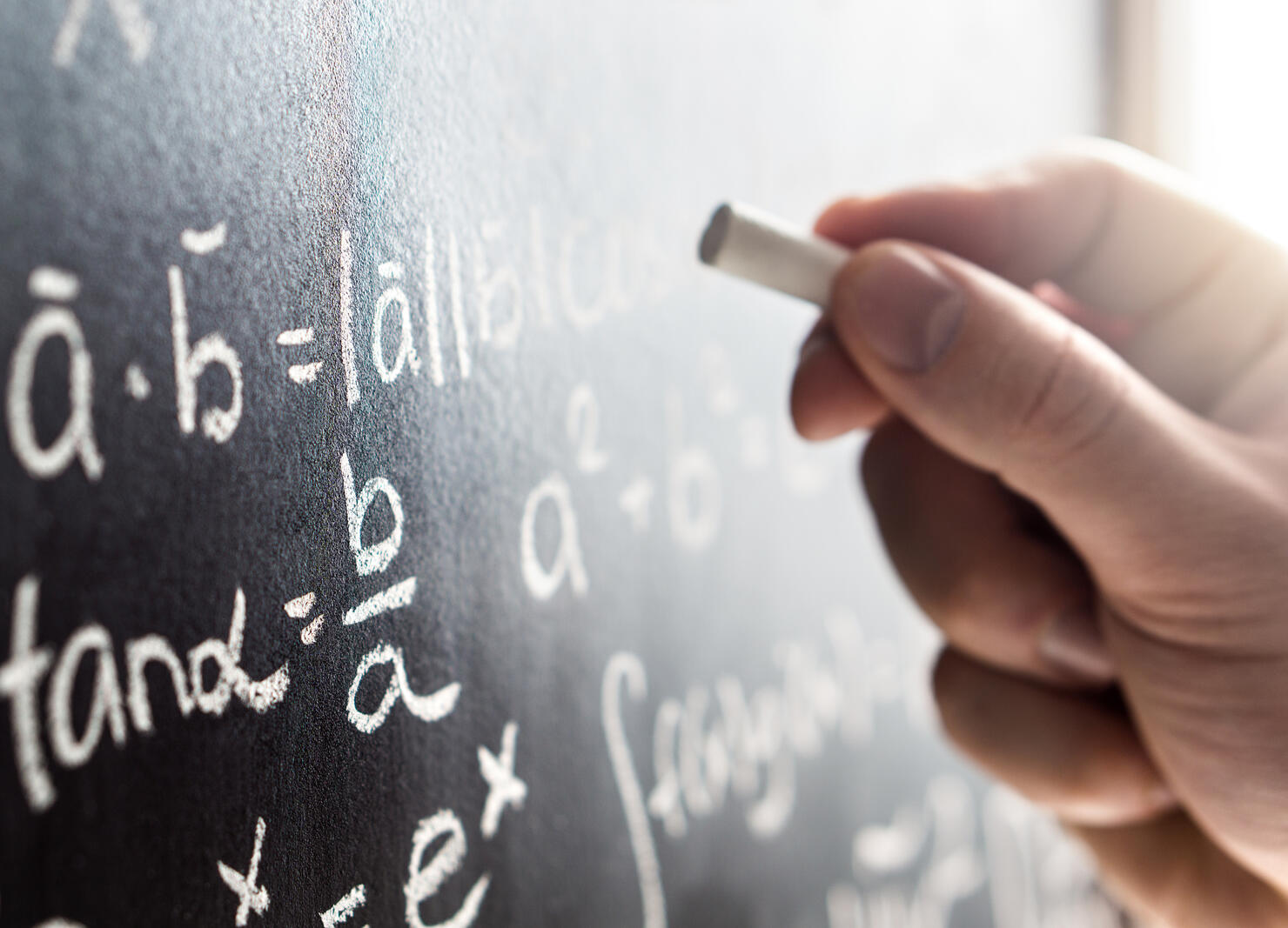 Teacher writing to blackboard with chalk. Student and chalkboard. Professor in school, college or university classroom.