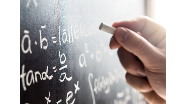 Teacher writing to blackboard with chalk. Student and chalkboard. Professor in school, college or university classroom.