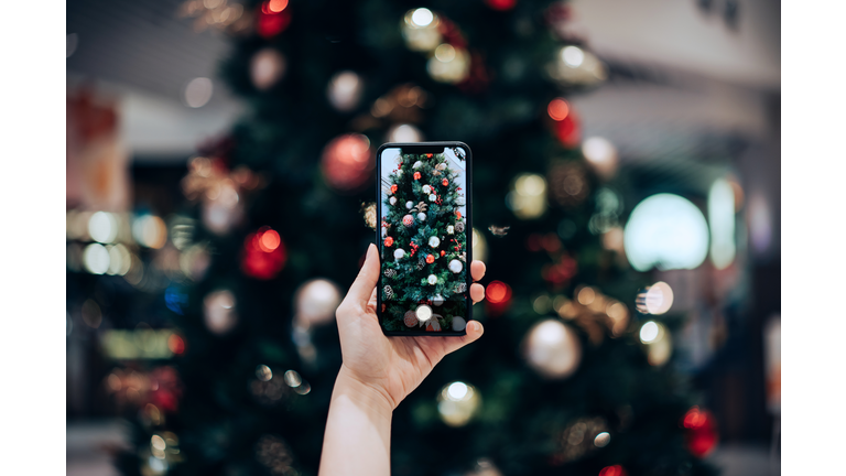 Personal perspective of woman's hand taking photo of a colourful Christmas tree with smartphone in the festive Christmas season