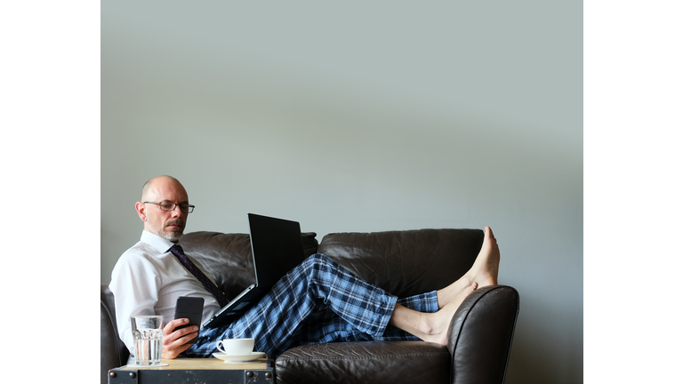 Businessman Working From Home On Couch In Dress Shirt And Pyjama Pants With Laptop And Mobile Smartphone, Stuttgart, Germany