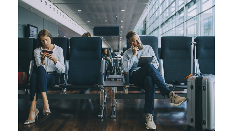 Thoughtful businessman looking away while sitting by female colleague at waiting area in airport