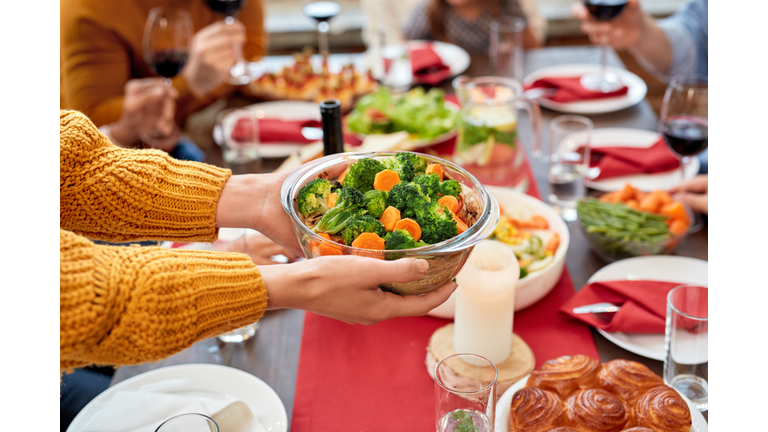 Woman holding bowl full vegetables over served dinner table