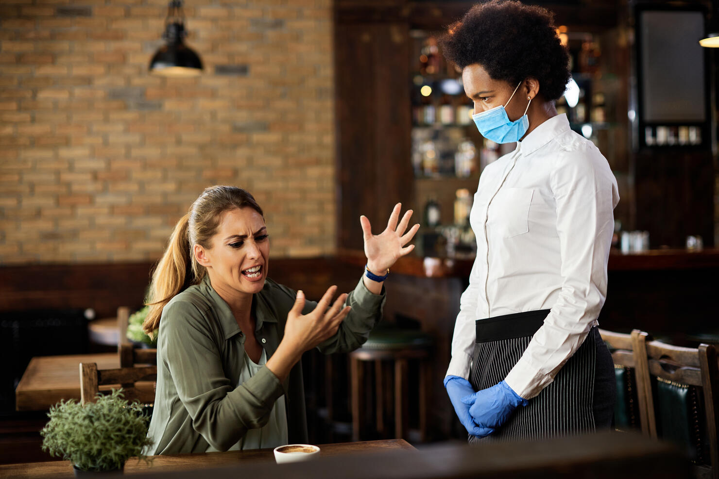 Upset woman having an argument with African American waitress in a cafe.
