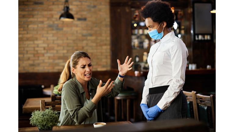 Upset woman having an argument with African American waitress in a cafe.