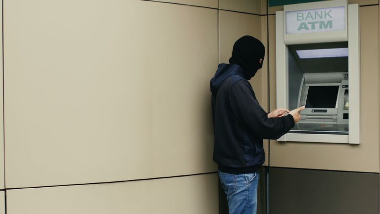 Hacker or thief with smartphone steals information or data from bank ATM