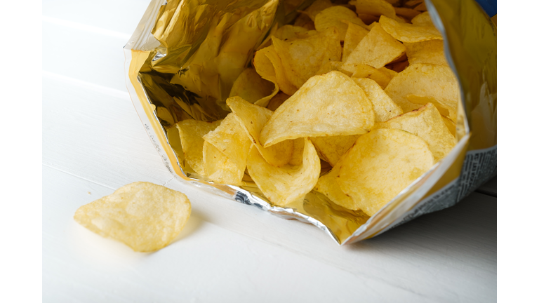 Crispy Fried Greasy Potato Chips fall out or are spilled out of the package, on a white background or table. The concept of unhealthy diet and lifestyle, accumulation of excess weight.