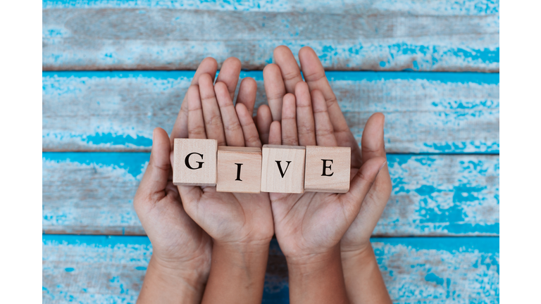 Alphabet letter wooden blocks with words GIVE in child and parents hands. Family and charity concept