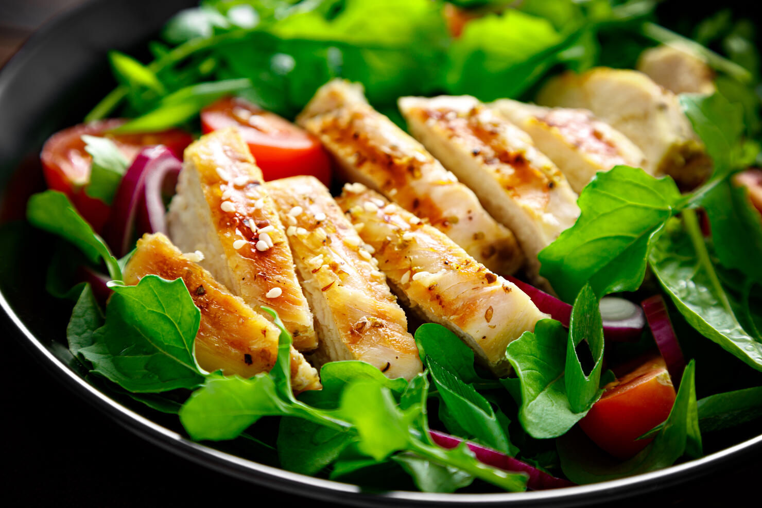 Grilled chicken breast and salad. Fresh vegetable salad with tomato, arugula, spinach and grilled chicken meat in bowl, healthy food.