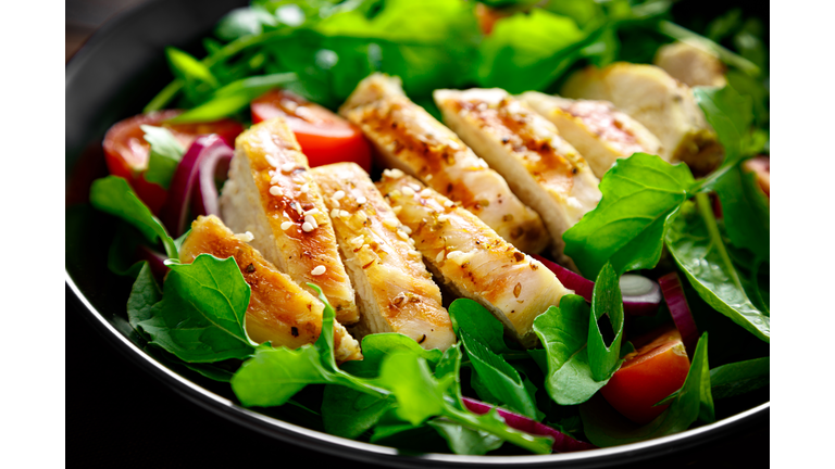 Grilled chicken breast and salad. Fresh vegetable salad with tomato, arugula, spinach and grilled chicken meat in bowl, healthy food.