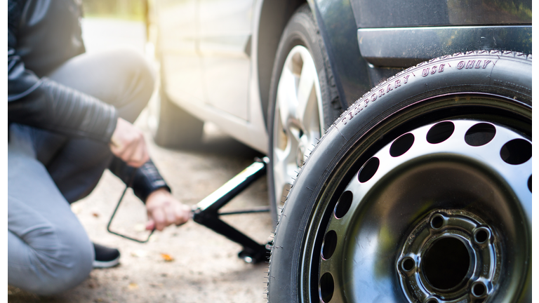 Driver changing spare tyre after accident. Broken and flat car wheel after crash. Man fixing problem with jack.