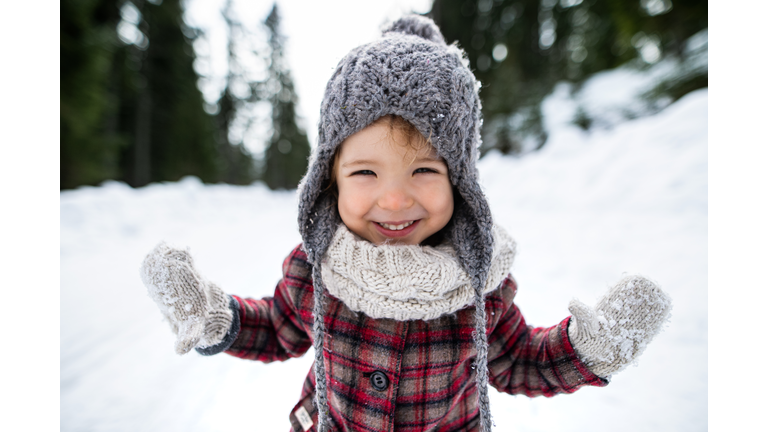 Front view portrait of cheerful small girl standing in winter nature, looking at camera.