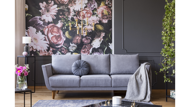 Industrial golden pendant light and black furniture in a dark living room interior with floral wallpaper and a gray couch