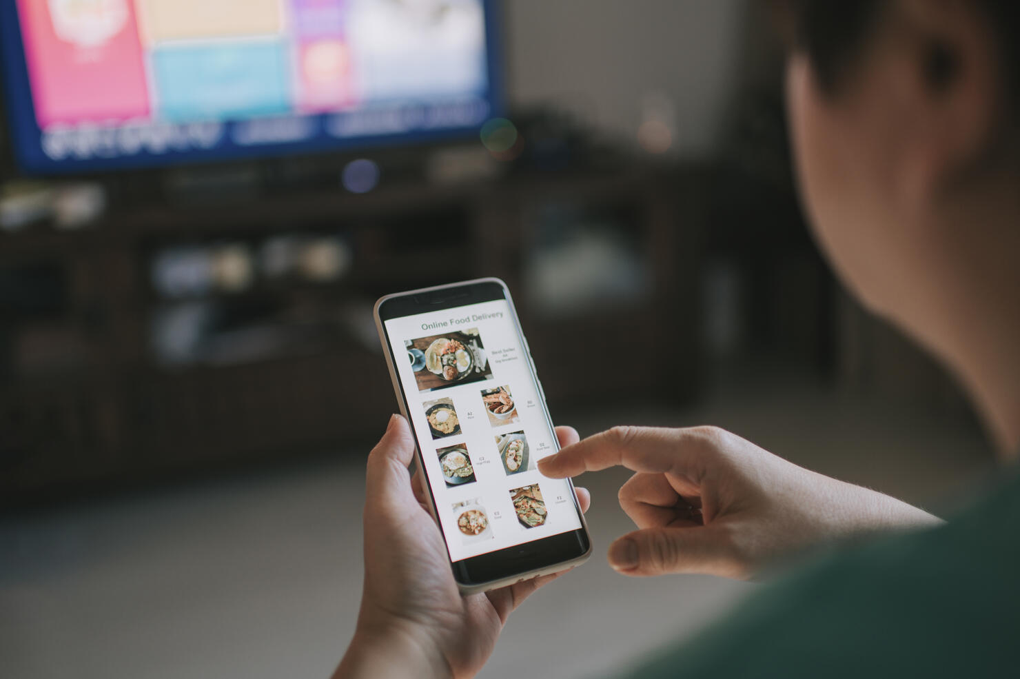 Online food delivery mobile app shown on smart phone screen hold by asian woman hands in living room
