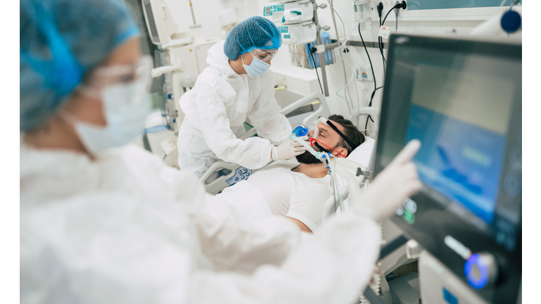 Coronavirus covid-19 infected patient in a quarantine ward at the hospital with doctors in protective suits while they making disease treatment of him