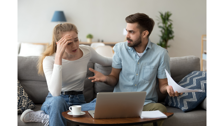 Stressed unhappy couple arguing about expenses with laptop and papers