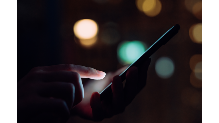 Close up of woman's hand using smartphone in the dark, against illuminated city light bokeh