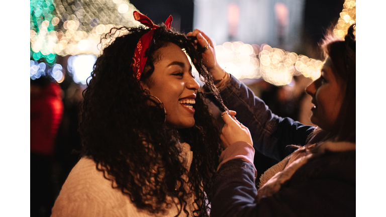 Happy young woman standing with girlfriend in city during Christmas