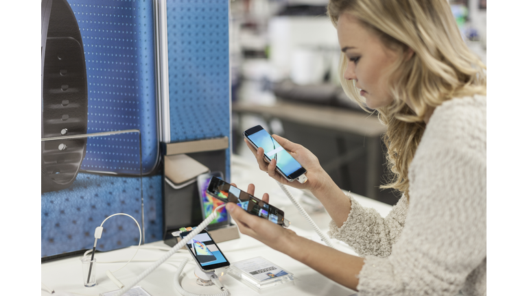 Young woman comparing two smartphones in a shop
