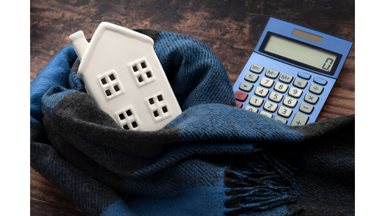 Warming efficiency of a residence and calculate heating costs concept with digital calculator, small house wrapped in warm wool neck scarf on wood background