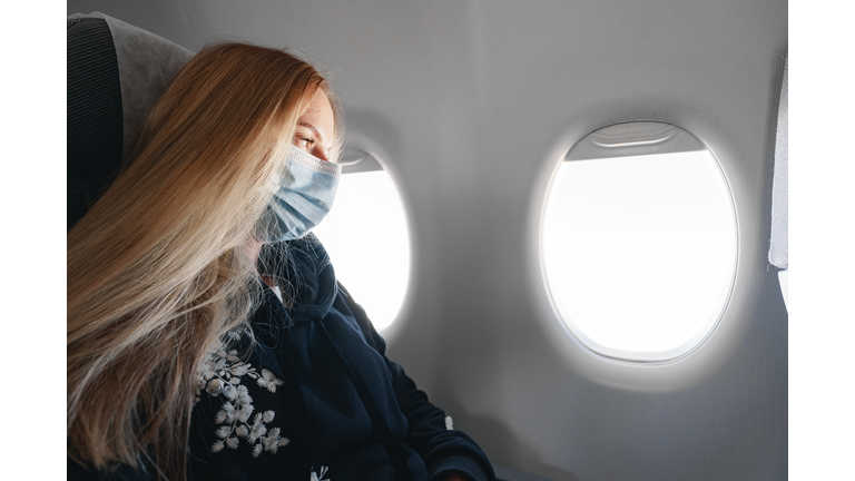 Blonde woman in medical mask sitting in the plane by the window