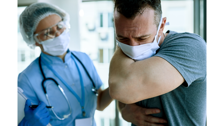 Ill man coughing into elbow while having appointment with doctor in the hospital.