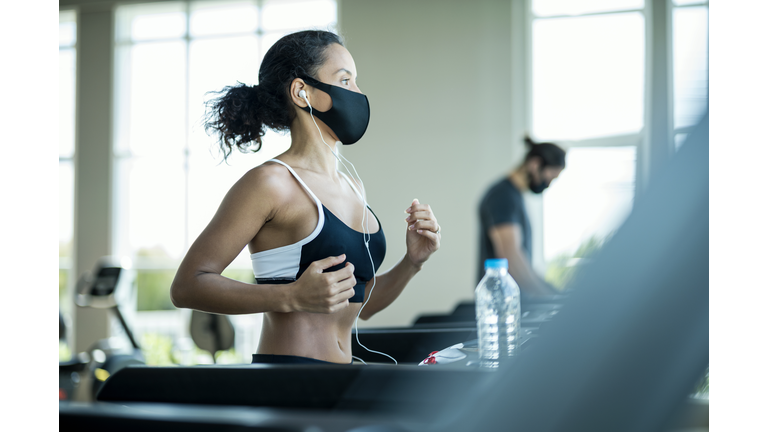 Athlete workout exercise at gym after pandemic reopening. They are running on treadmill and wearing protect facemask during virus protection.