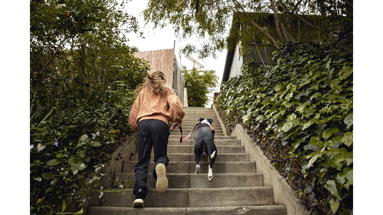 Young girl running up steps while walking dog