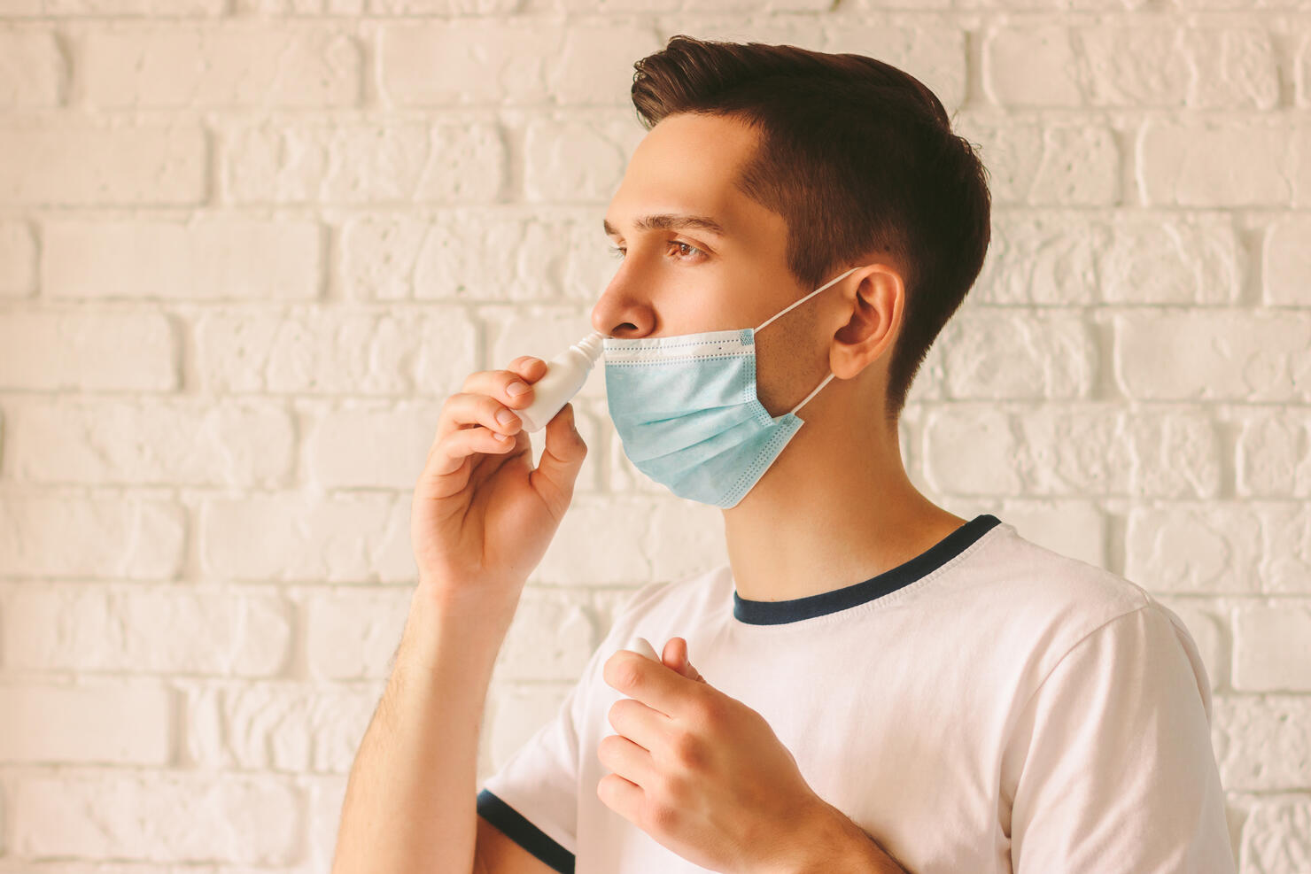 Sick young man using nose drops for congested nose