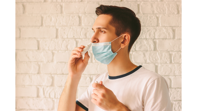 Sick young man using nose drops for congested nose