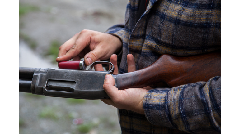 Close up of man loading a red shotgun shell into the magazine of his gun