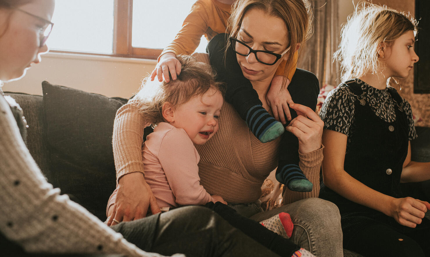 A busy single Mum of 4 comforts a crying toddler while surrounded by older children